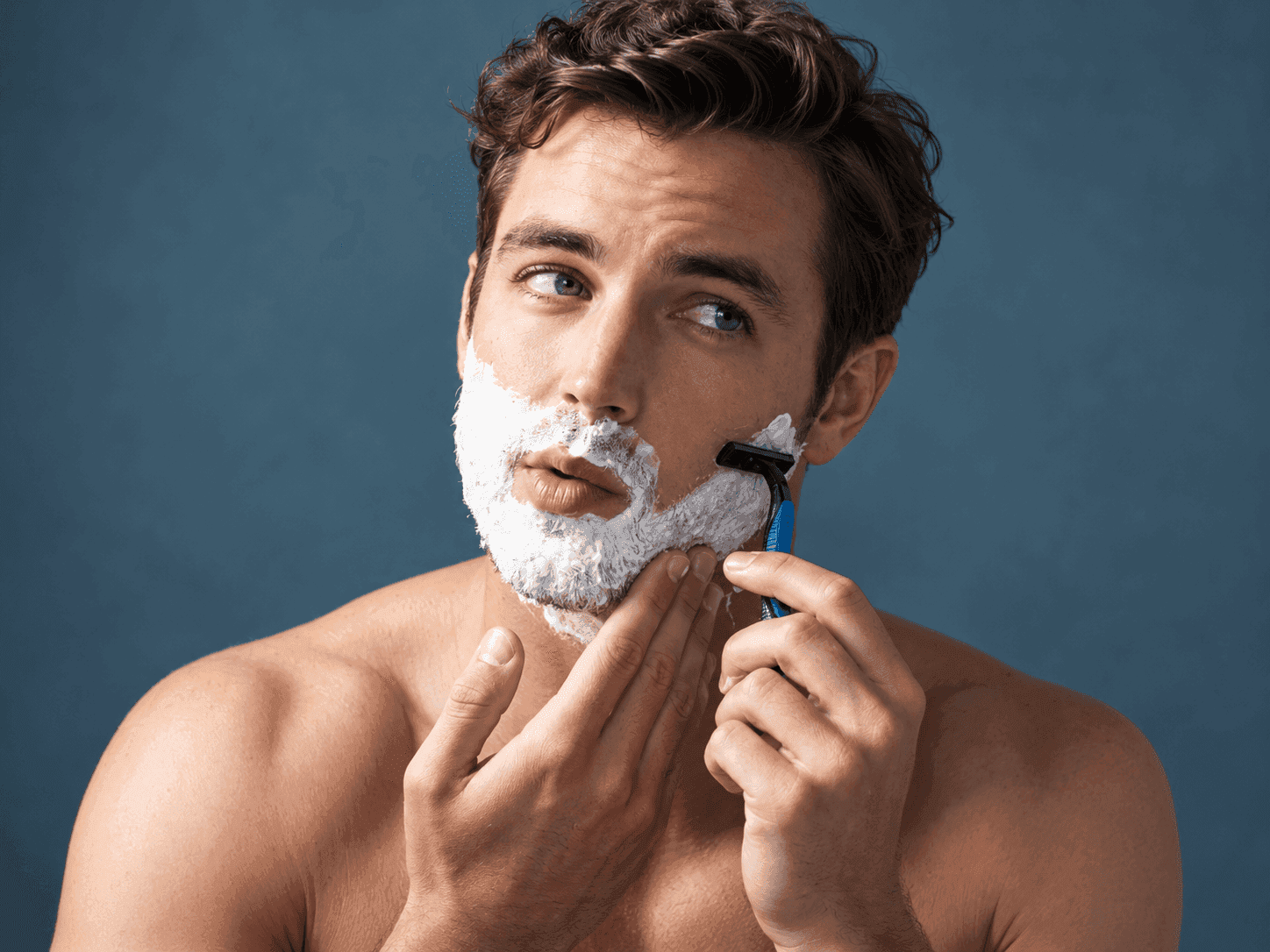 Man shaving face against blue background